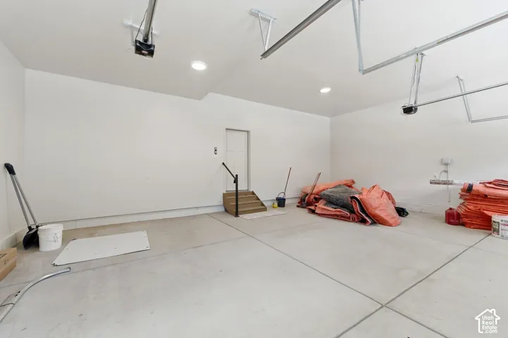 Spacious garage featuring a concrete floor, white painted walls, recessed lighting, two garage door openers, and a utility door with adjacent wood steps and a black handrail
