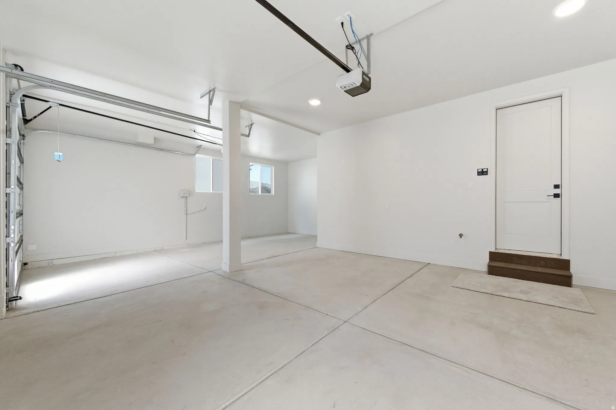 Spacious garage with concrete flooring, automatic garage door opener, a side entry door with wood-finish steps, and recessed lighting