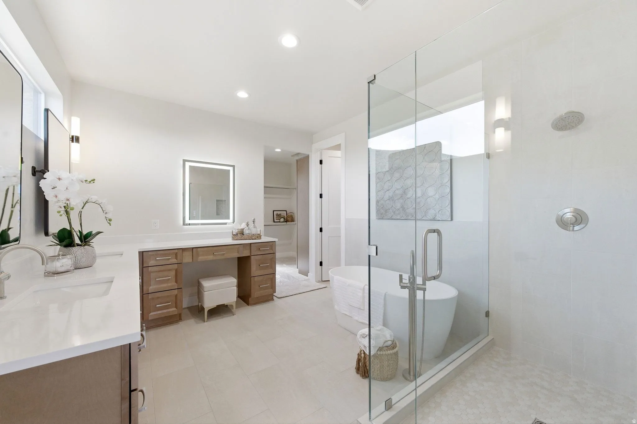 Spacious bathroom featuring a frameless glass shower enclosure, a freestanding soaking tub, dual vanities with integrated sinks, wood-finish cabinetry, and a dedicated makeup vanity with illuminated mirror