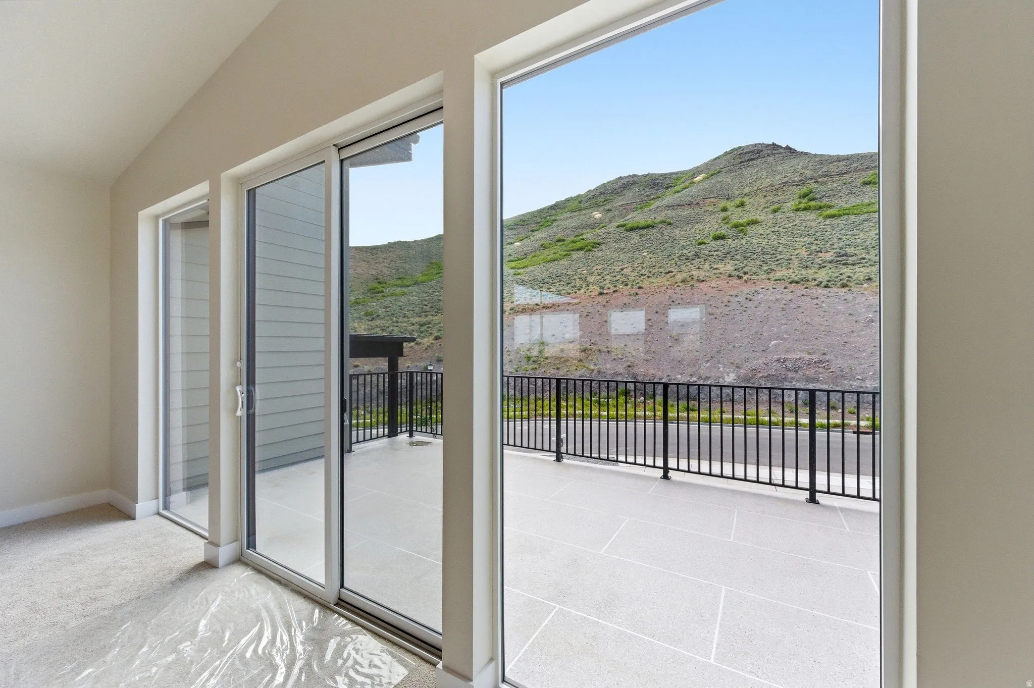 Spacious room with sloped ceilings and light-toned walls, featuring a sliding glass door and two fixed glass panels opening to an outdoor patio