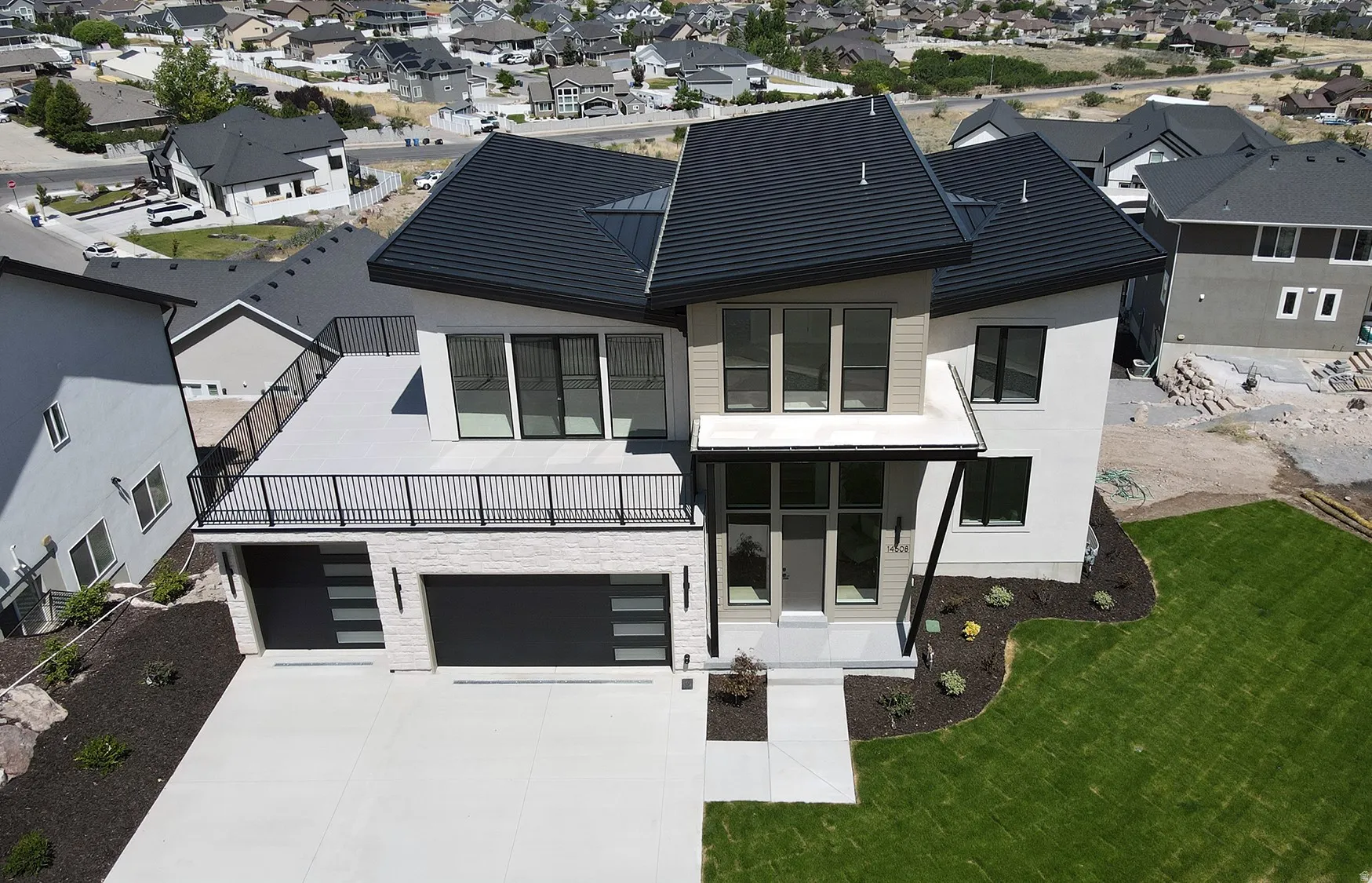 Contemporary residence featuring a striking black metal roof and a spacious upper-level balcony with black iron railings
