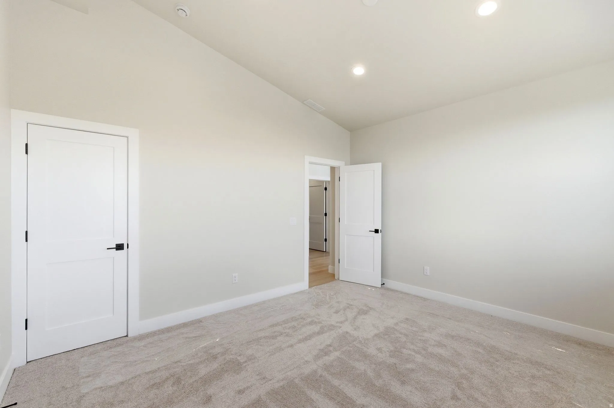 Spacious room featuring neutral carpeting, light-colored walls, recessed ceiling lights, and white solid panel doors with matte black hardware