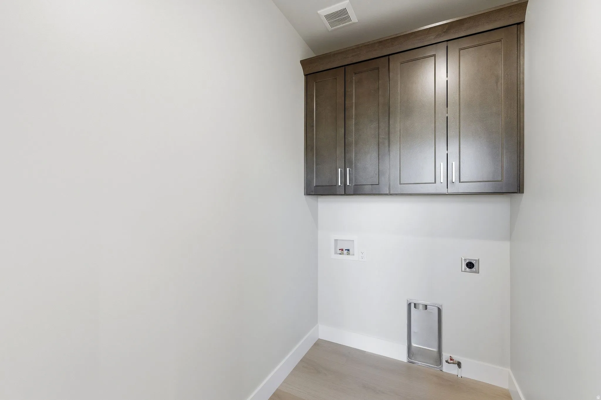 Laundry area featuring wood-finish flooring, white baseboards, and built-in upper cabinetry with brushed nickel hardware