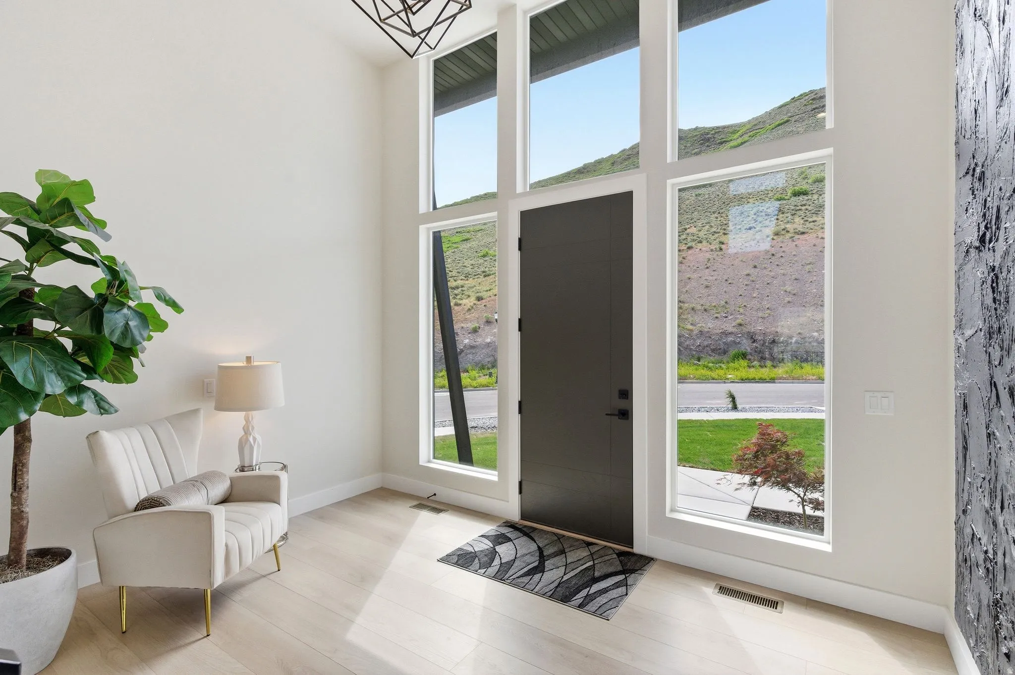 Two-story entryway featuring wood-finish flooring, a black entry door, and multiple floor-to-ceiling windows