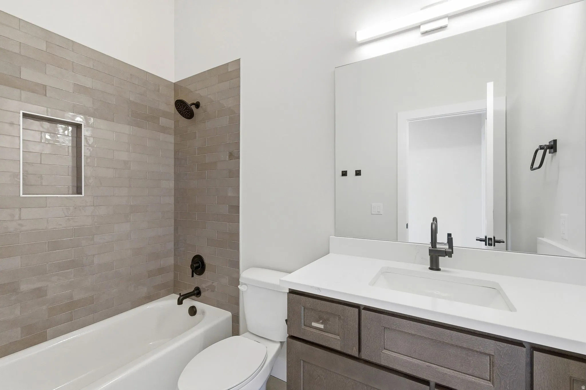 Bathroom featuring an integrated tub with subway tile surround, matte black fixtures, and a recessed shower niche