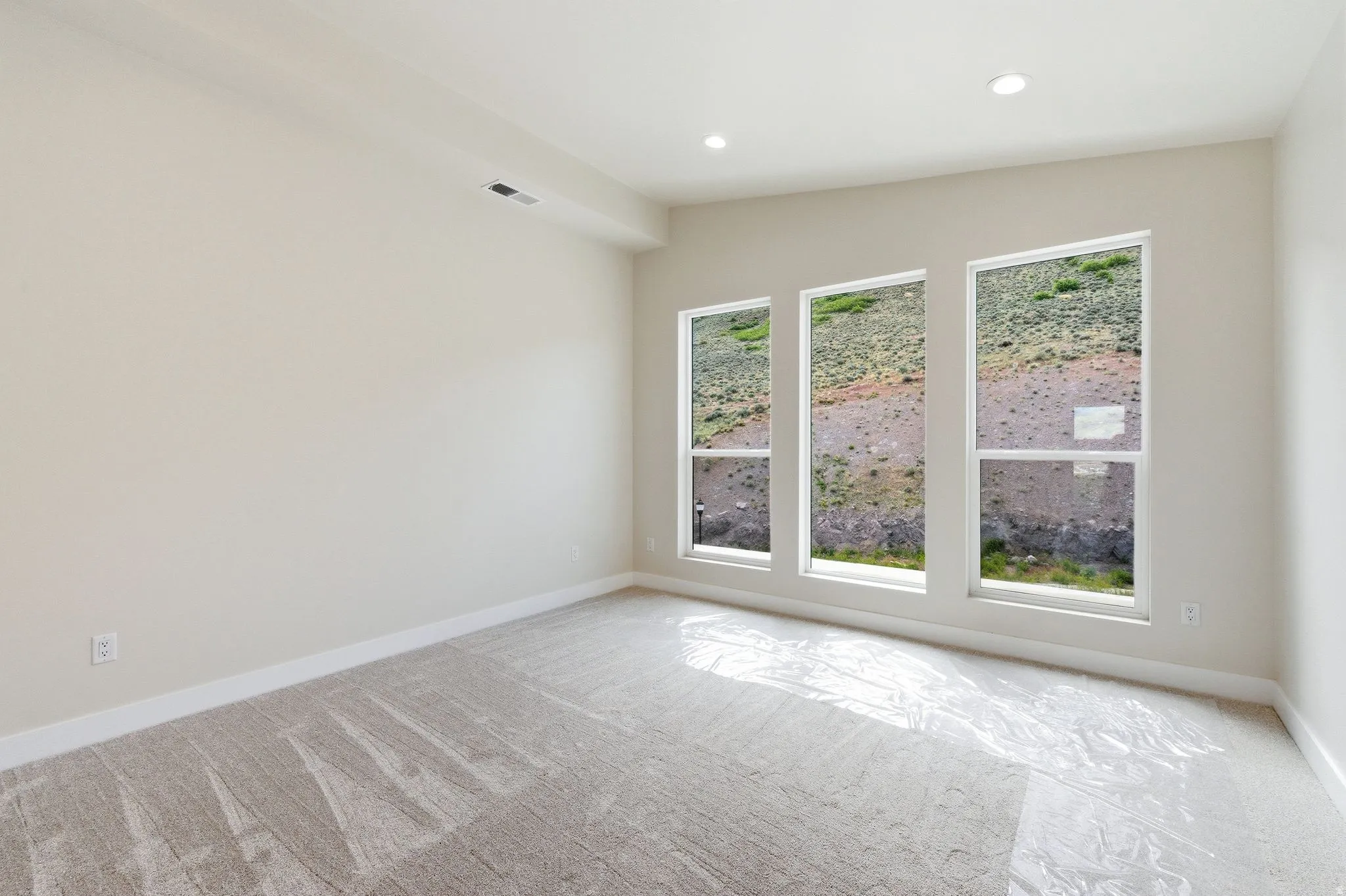 Spacious room featuring three large windows, recessed lighting, neutral wall paint, white baseboards, and light-toned carpet