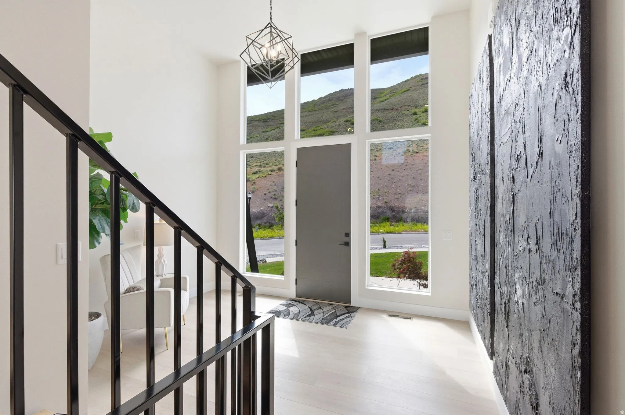 Two-story entryway featuring a black geometric chandelier, a full-light entry door, and a black metal staircase railing
