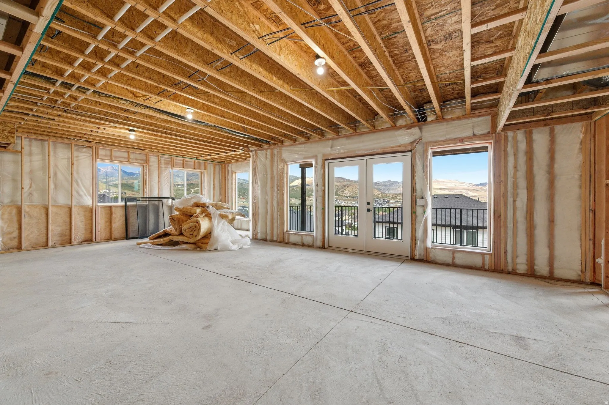 Unfinished lower level featuring exposed wood joists and subfloor, concrete flooring, multiple windows providing natural light, and a double patio door with an exterior balcony