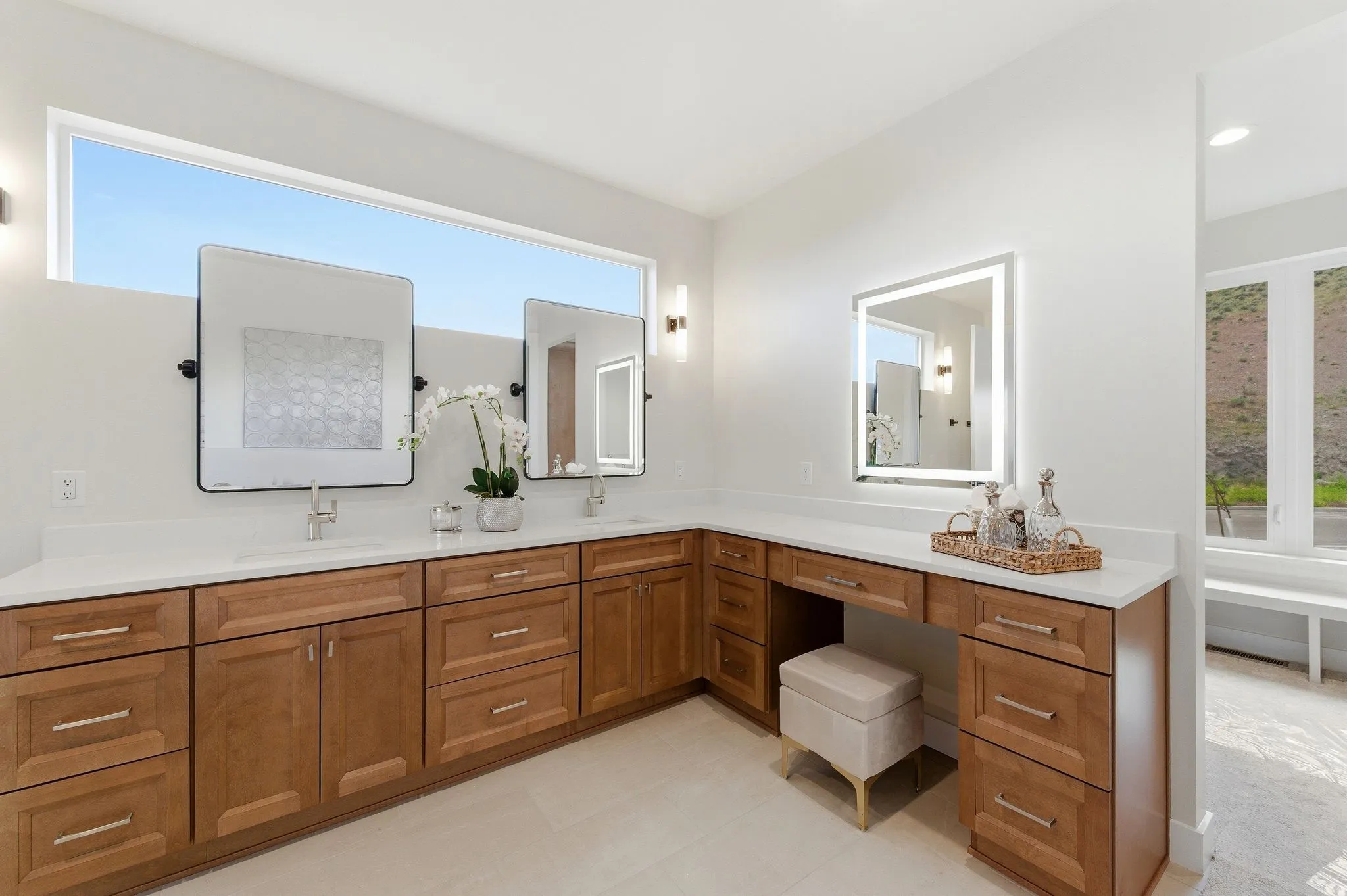 Spacious vanity area featuring light wood cabinetry with brushed nickel hardware, dual undermount sinks, and white countertops