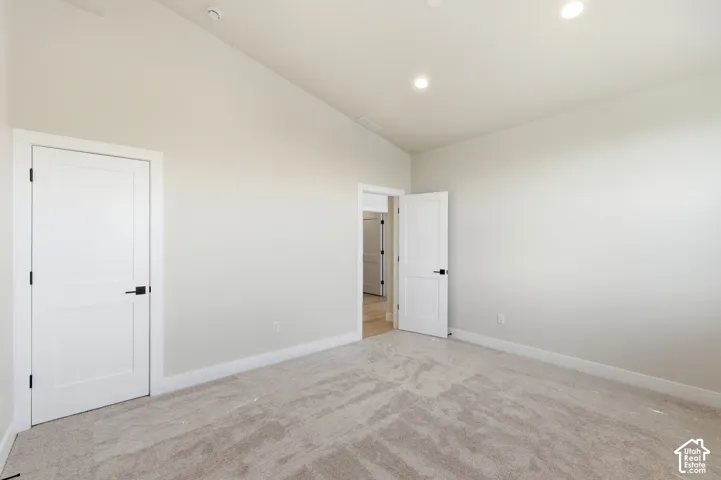 Spacious room featuring neutral carpeting, light-colored walls, recessed ceiling lights, and white solid panel doors with matte black hardware