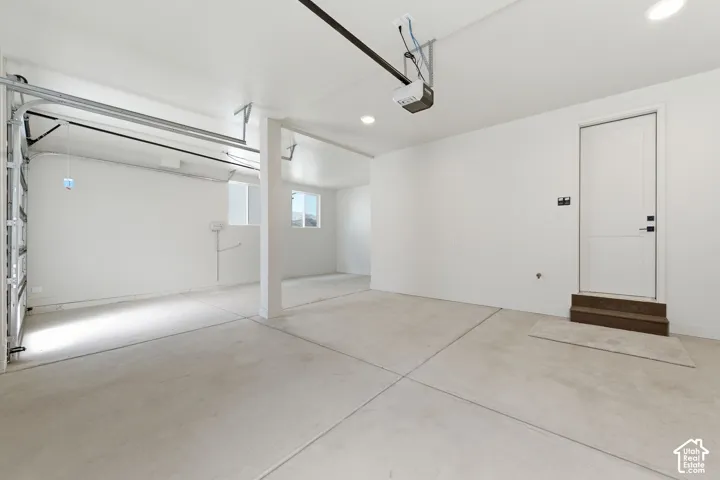 Spacious garage with concrete flooring, automatic garage door opener, a side entry door with wood-finish steps, and recessed lighting