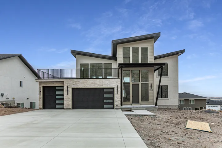 Contemporary exterior featuring a multi-level design, a two-car garage with frosted glass panels, a stone facade, and a second-story balcony with metal railings