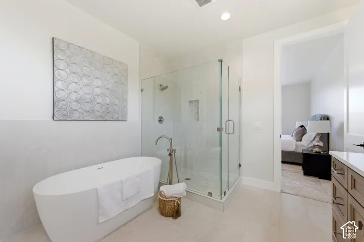 Spacious bathroom featuring a freestanding soaking tub, a glass-enclosed shower with built-in niche, light-toned wall tile, wood-finish vanity with countertop, and recessed lighting