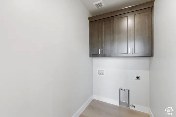 Laundry area featuring wood-finish flooring, white baseboards, and built-in upper cabinetry with brushed nickel hardware
