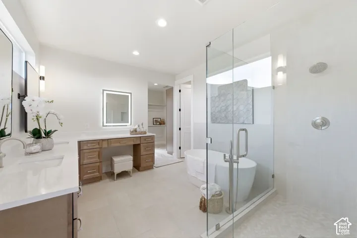 Spacious bathroom featuring a frameless glass shower enclosure, a freestanding soaking tub, dual vanities with integrated sinks, wood-finish cabinetry, and a dedicated makeup vanity with illuminated mirror
