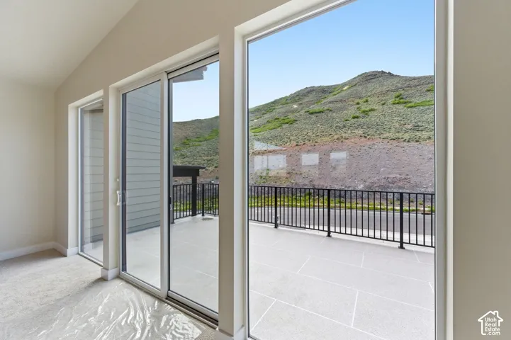 Spacious room with sloped ceilings and light-toned walls, featuring a sliding glass door and two fixed glass panels opening to an outdoor patio