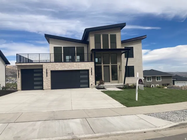 Modern architectural home featuring a prominent two-car garage with frosted glass panel doors, a stone facade, and a second-story balcony with dark railings