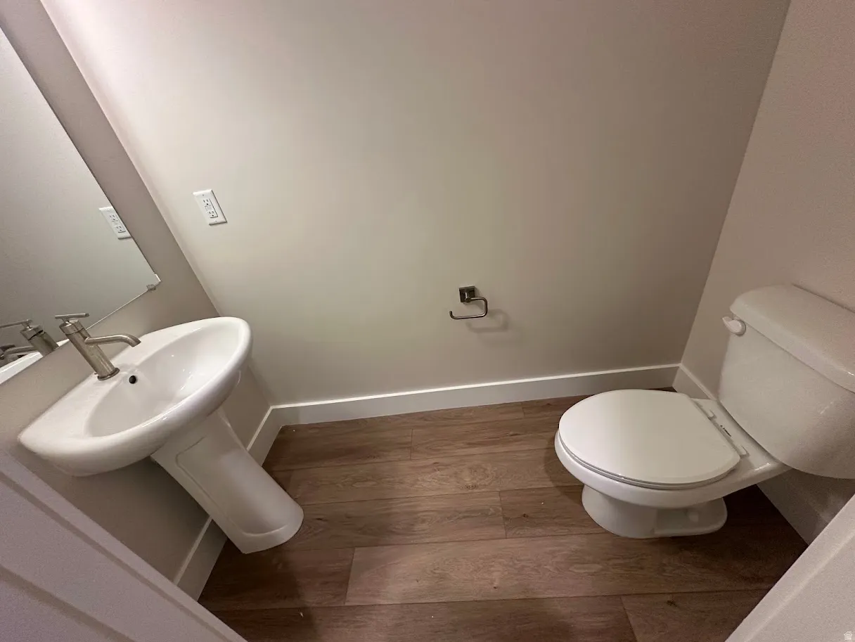 Pedestal sink with a brushed nickel faucet, large wall mirror, white toilet, and wood-finish flooring