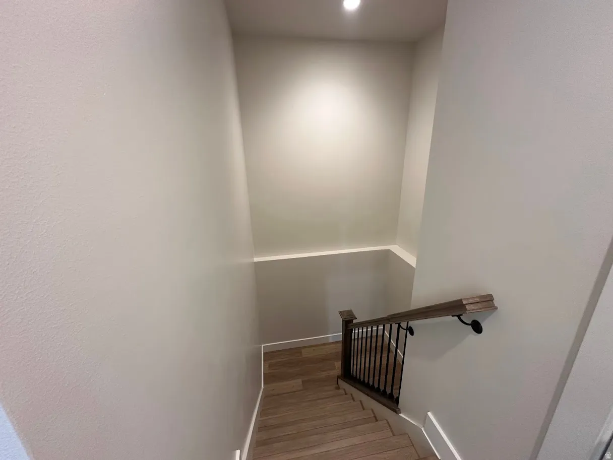 Stairway featuring wood-finish treads, a dark wood-finish handrail, black metal balusters, and recessed lighting