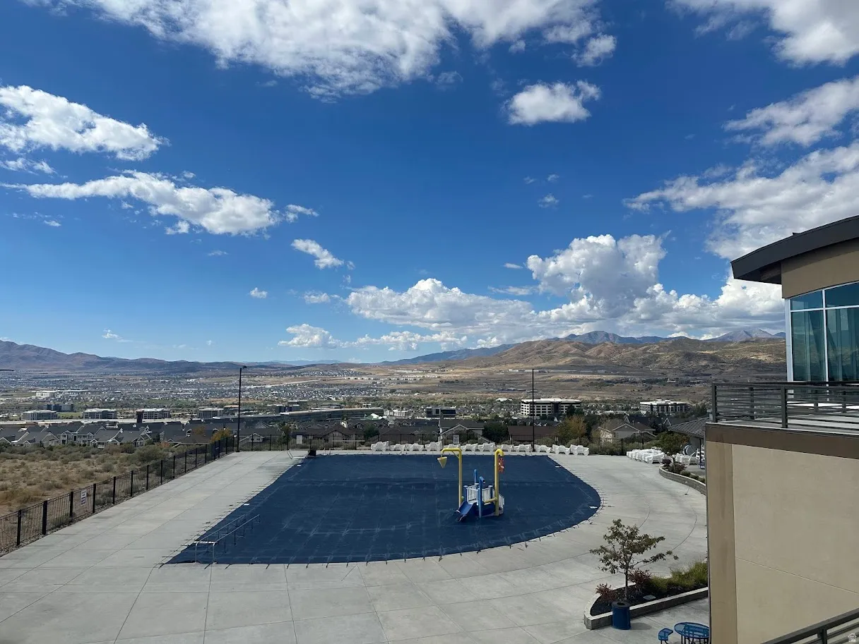 Outdoor pool area featuring a dark blue pool cover, surrounding concrete patio, and security fencing
