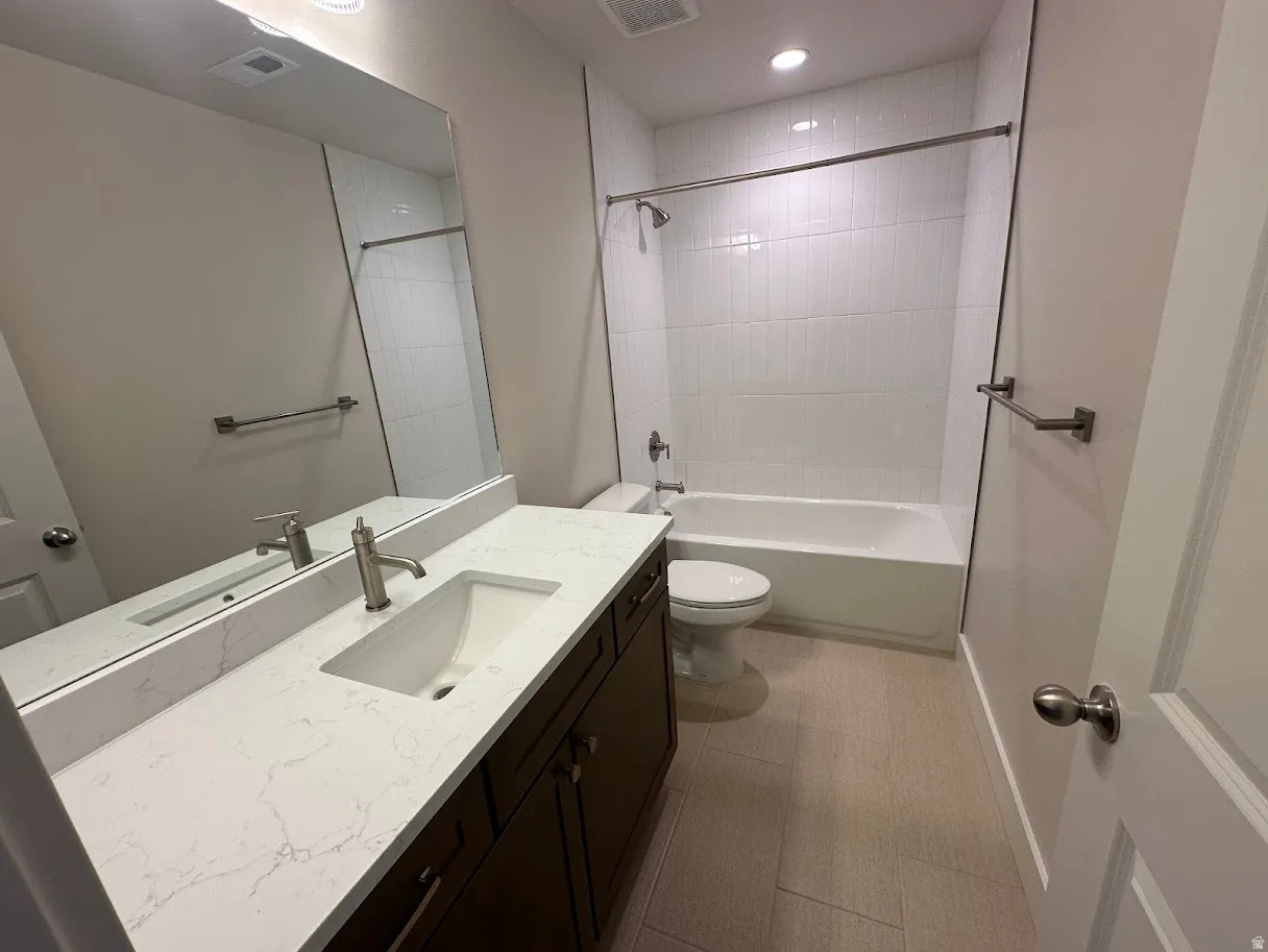 Bathroom featuring a white bathtub, a single vanity with a white countertop and integrated sink, dark wood-finish cabinetry, and light-toned floor tiling