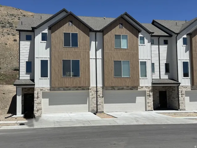 Modern multi-story townhome featuring a stone and siding exterior, a two-car garage, and multiple windows across the facade