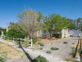Ranch-style residence featuring a stone exterior, a white picket fence, mature trees, and a two-car garage with a paved driveway
