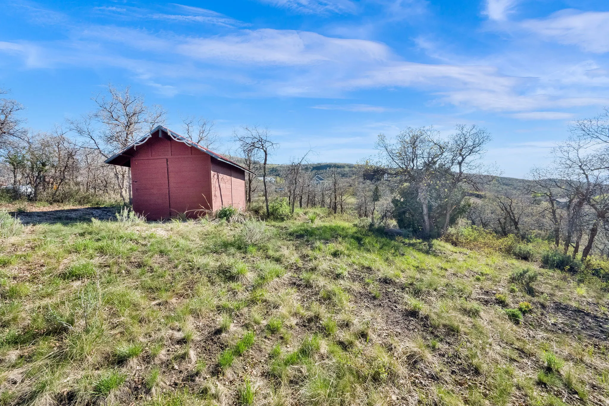 Red-sided outbuilding with a corrugated metal roof on a sloped, grassy terrain