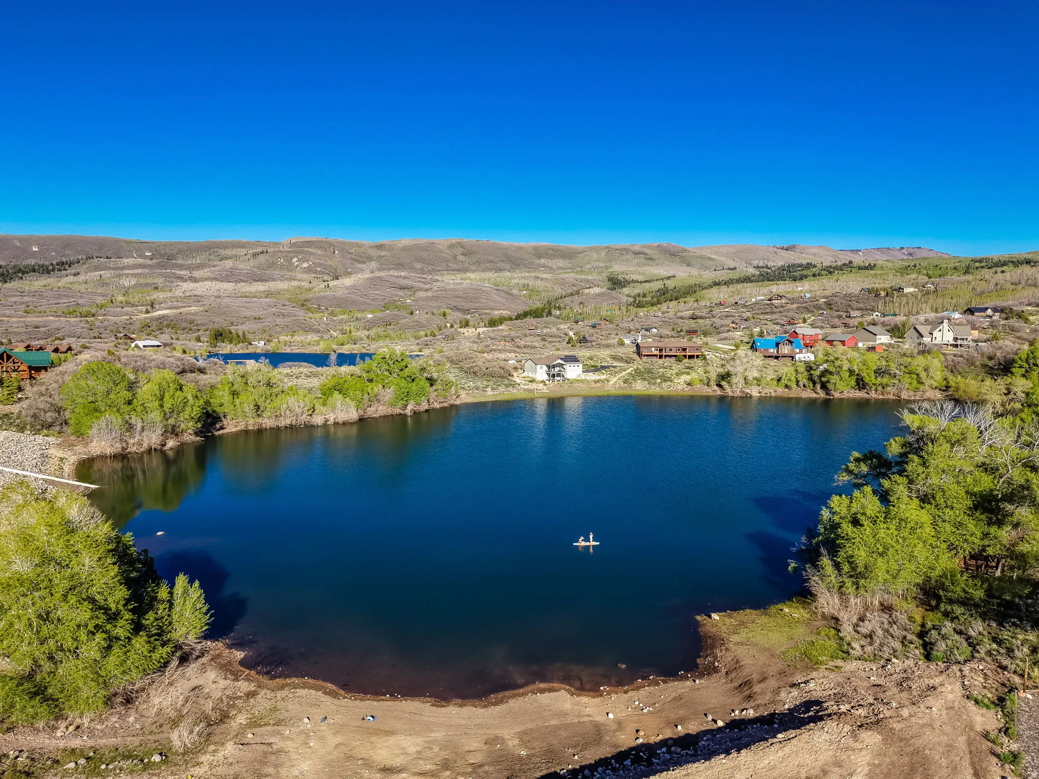 Expansive lakefront property featuring a private lake, surrounding natural landscape, and distant residential structures