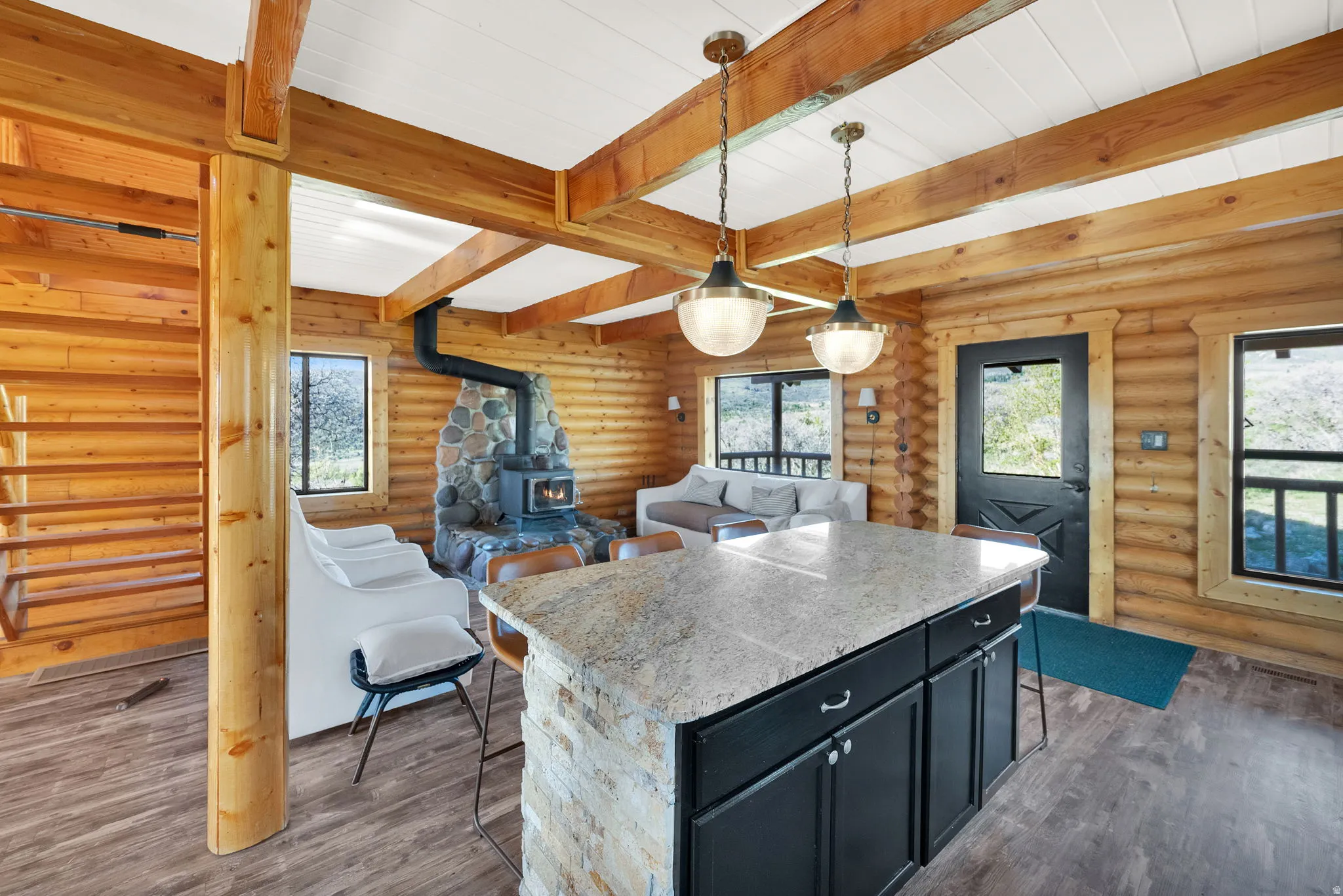 Open-concept living space featuring wood-finish flooring, exposed wood beams, and log walls