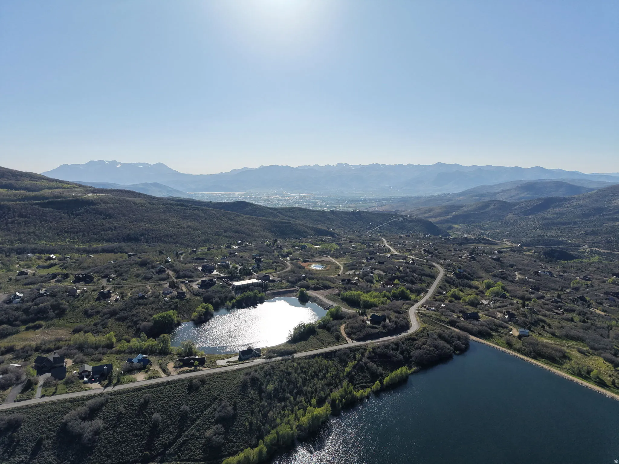 Expansive aerial perspective showcasing a mountainous landscape with a large body of water, a smaller reflective pond, and scattered residential properties throughout the hills