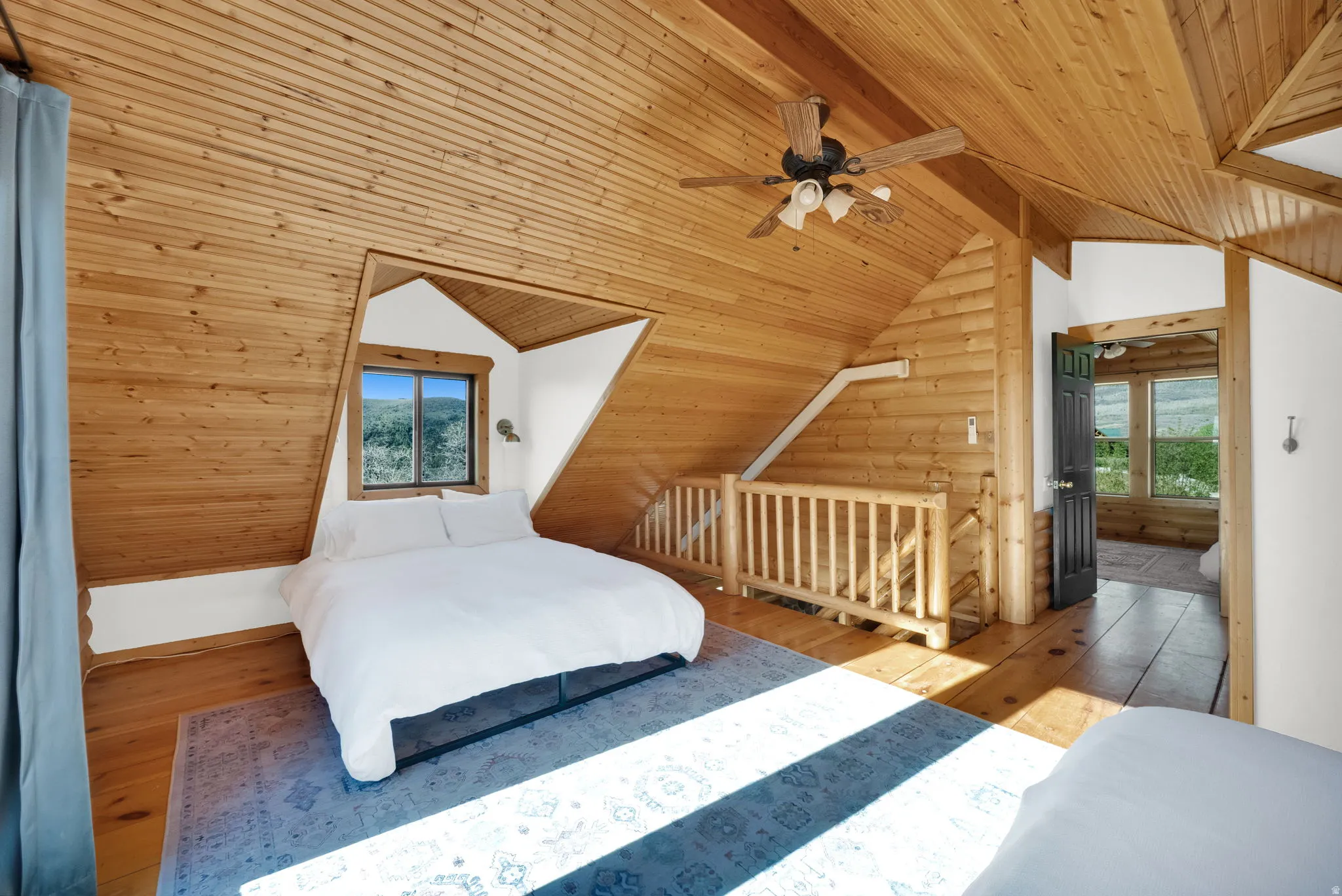 Attic bedroom featuring natural wood plank walls and ceiling, a window with exterior scenery, a ceiling fan with integrated lighting, and wood-finish flooring