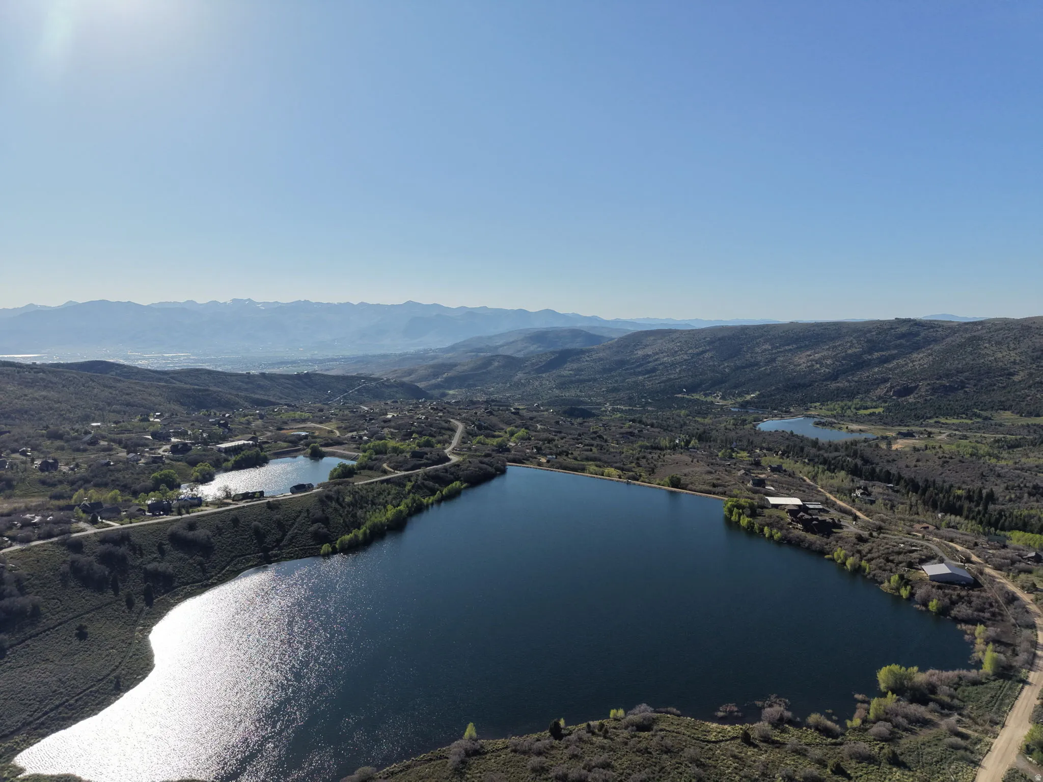 Aerial landscape featuring multiple lakes, surrounding hills, and distant mountains under a clear sky