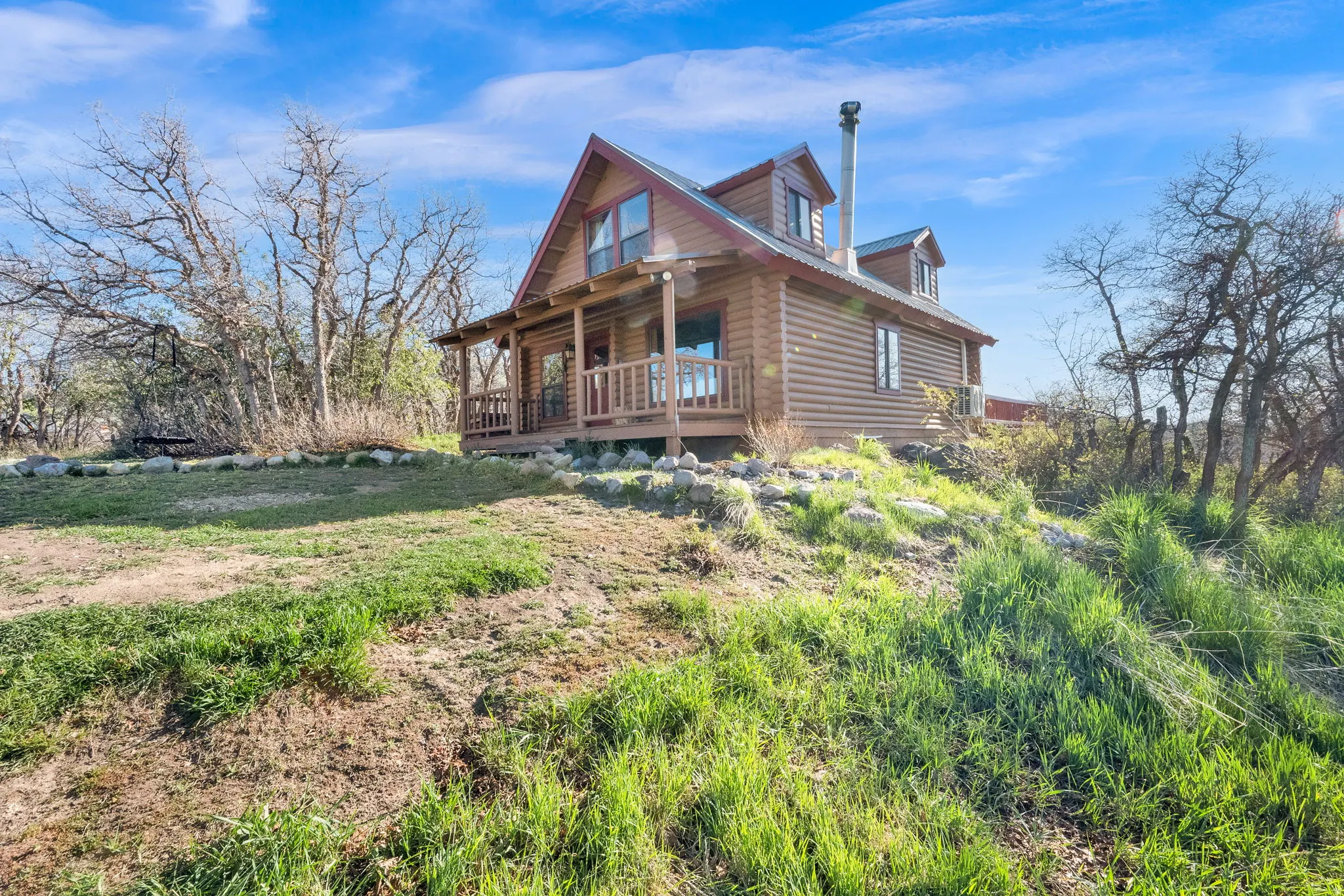 Log cabin exterior featuring a covered front porch with wood railings, a dormer window, and a metal chimney