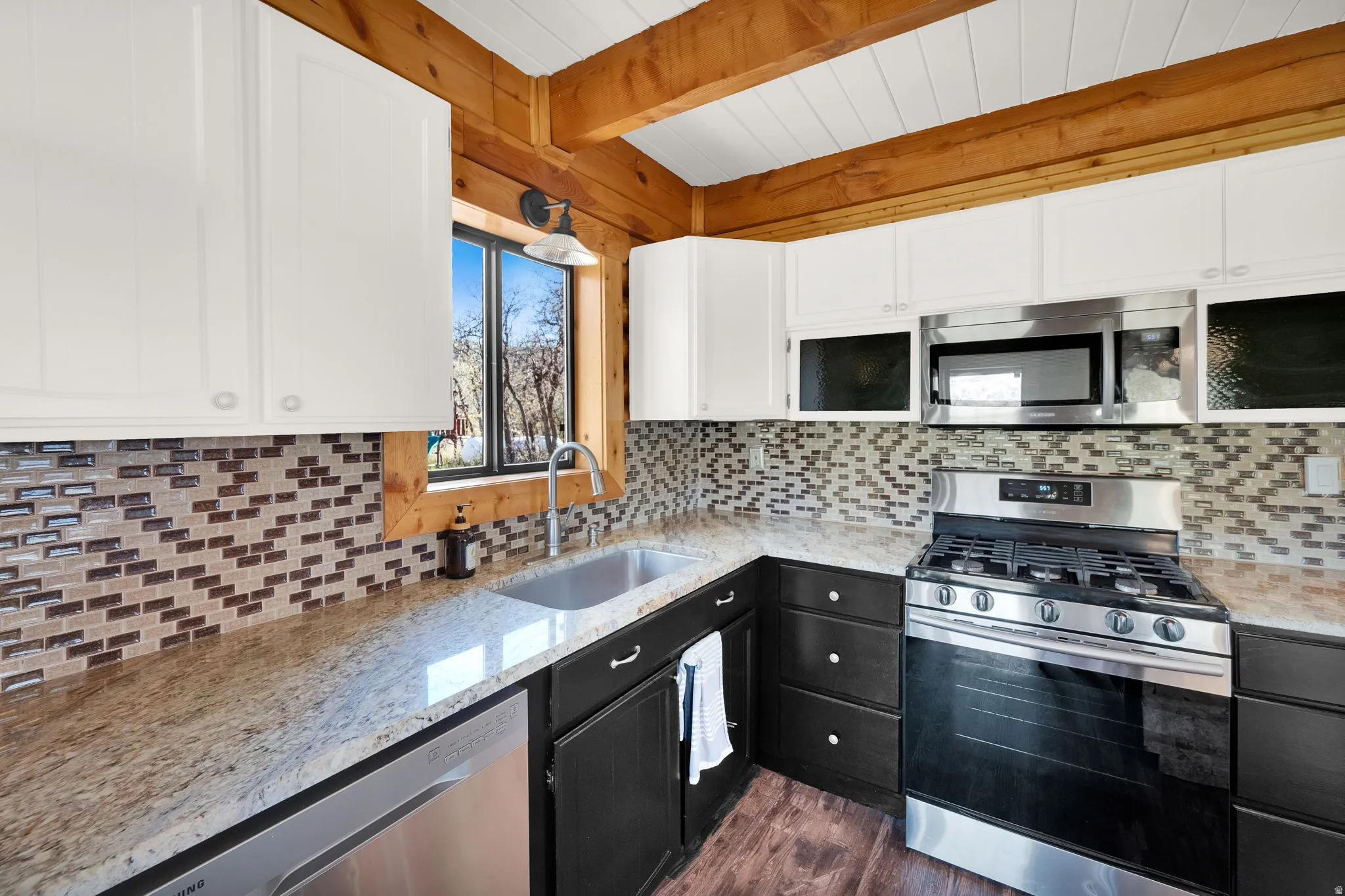 Wood-beamed ceiling with shiplap, granite countertops, tile backsplash, stainless steel appliances, and a stainless steel sink with a gooseneck faucet