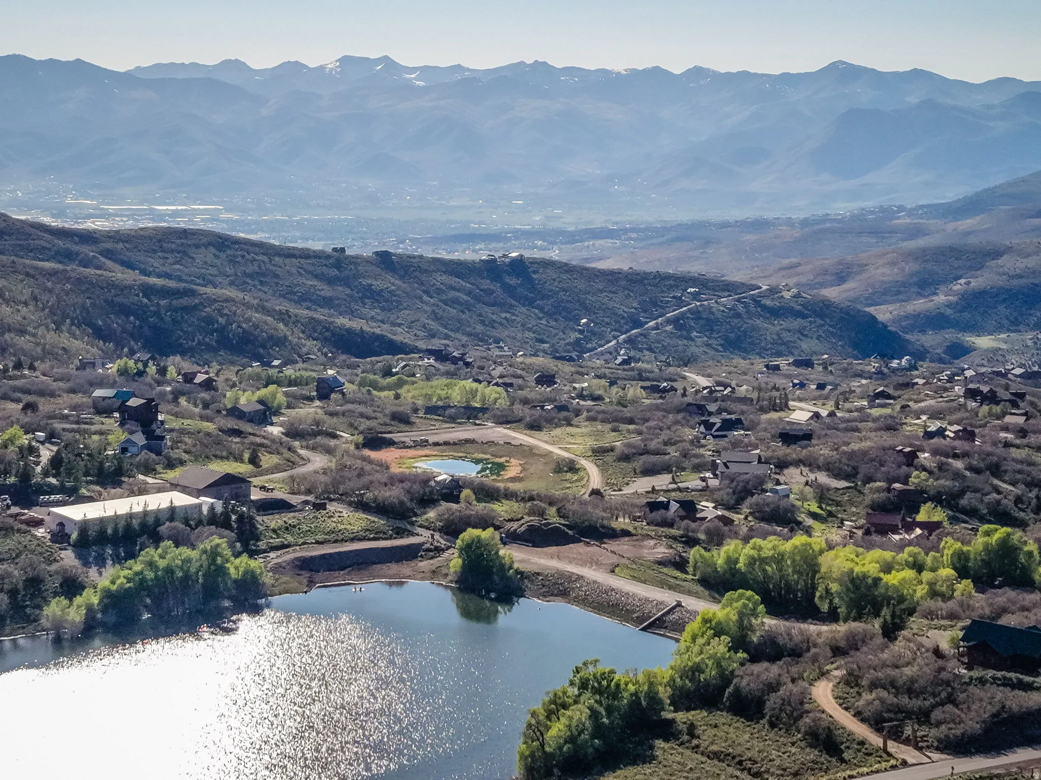 Aerial landscape featuring a tranquil lake, surrounding residential properties, and distant mountain ranges
