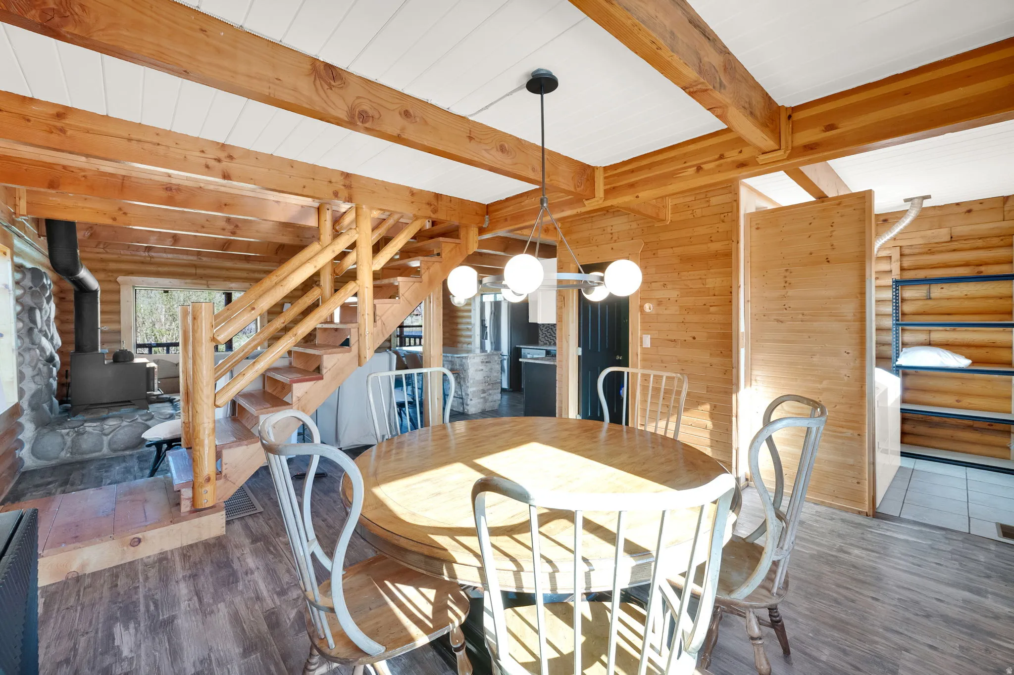 Open-concept interior featuring wood-finish flooring, exposed wood beams, and a prominent wood staircase