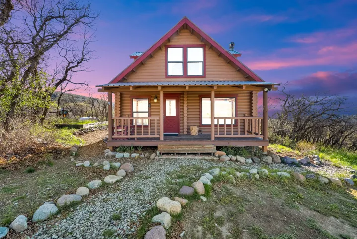 Log cabin exterior featuring a covered front porch, red entry door, and a metal roof