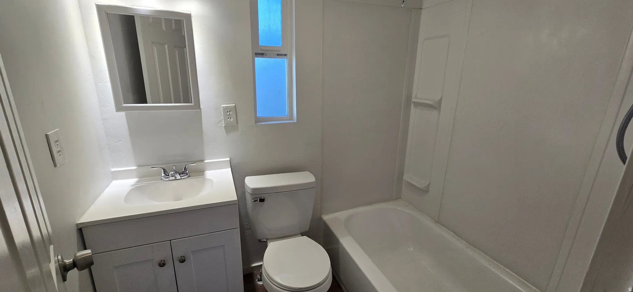 Bathroom featuring a white vanity with integrated sink, chrome faucet, wall-mounted mirror, and a toilet