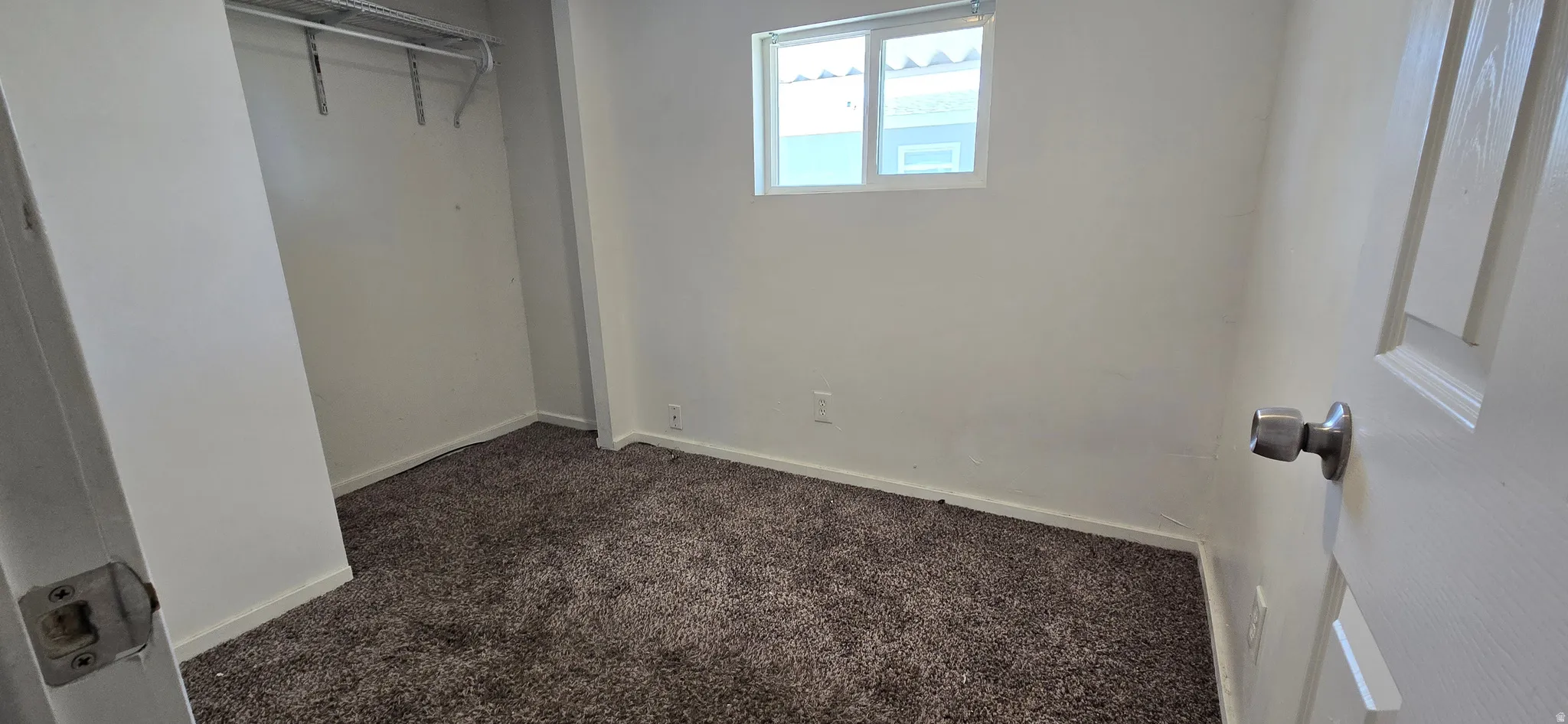 Carpeted room featuring white walls, a single window, and a closet with a built-in shelf and hanging rod