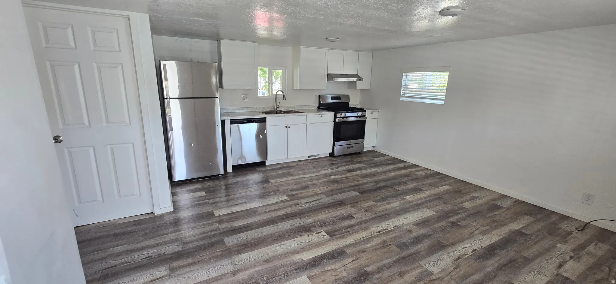 Contemporary kitchen featuring white cabinetry, stainless steel appliances, wood-finish flooring, and a window with blinds