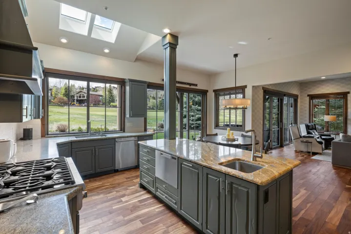 Open-concept kitchen featuring an oversized island with an undermount sink, stone countertops, gray cabinetry, stainless steel appliances, and wood-finish flooring