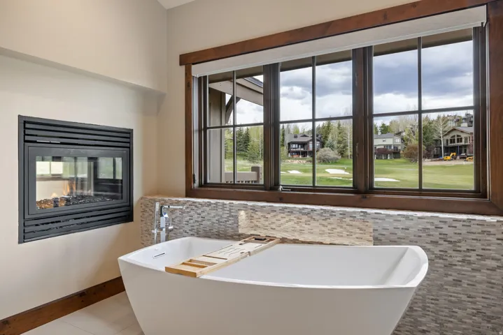 Freestanding soaking tub with a wall-mounted faucet, complemented by a mosaic tile backsplash and an inset fireplace