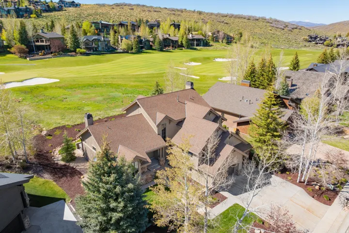 Multi-level property featuring a brown shingle roof, stone and siding exterior, multiple chimneys, a concrete driveway, and mature trees