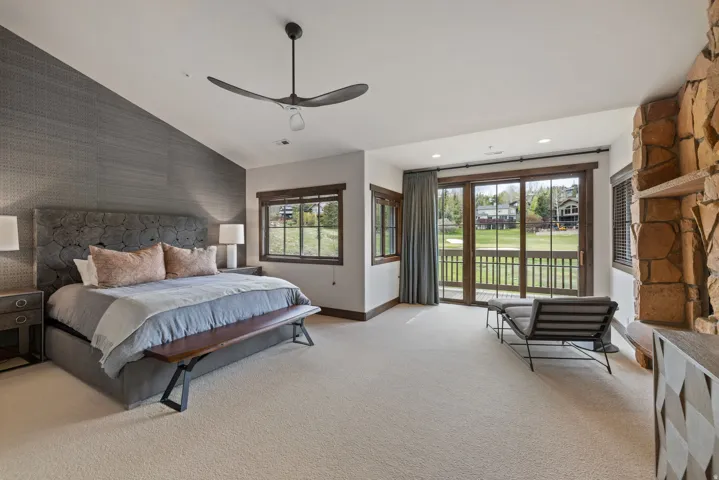 Spacious room featuring vaulted ceilings, a prominent stone-clad fireplace, and sliding glass doors opening to an outdoor deck