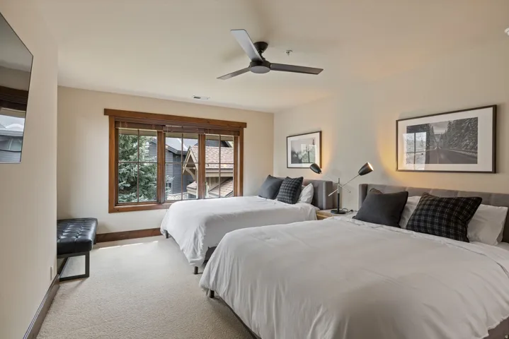 Carpeted room featuring a ceiling fan, wall-mounted television, and a window with wood trim