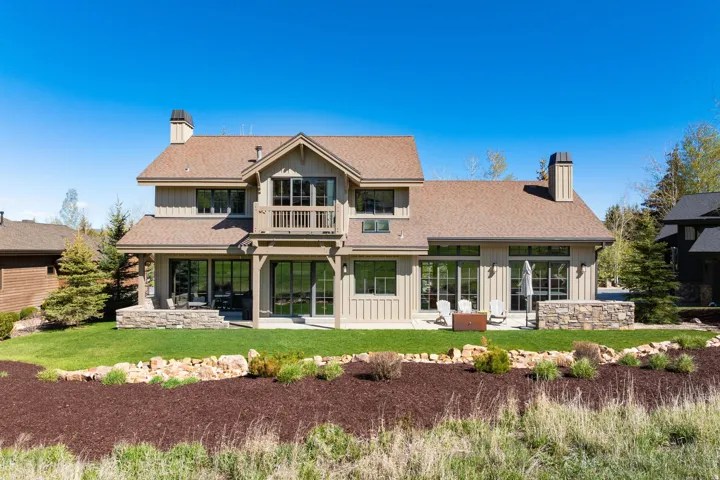 Rear exterior featuring multiple outdoor living spaces, expansive lawn, two stone chimneys, multiple large windows, and a second-story balcony