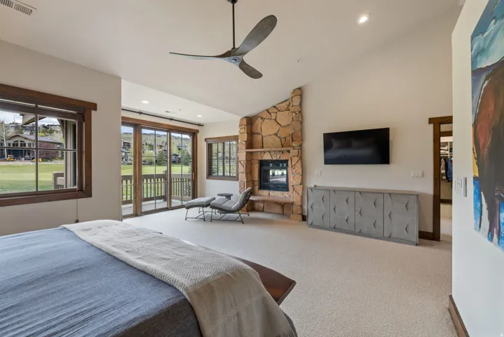 Spacious room featuring a stone-clad fireplace with a built-in television, a vaulted ceiling with a modern ceiling fan, and light-toned carpeting