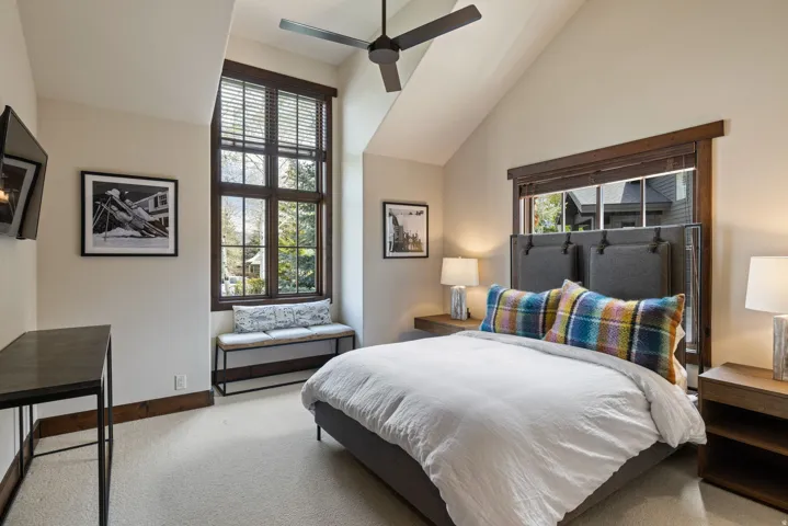 Vaulted ceiling bedroom featuring a large multi-pane window with dark wood trim, a built-in window bench, light-colored carpet, and an overhead ceiling fan