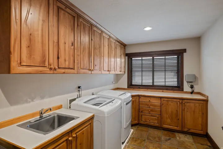 Spacious utility room featuring extensive wood cabinetry, light-toned countertops, a stainless steel utility sink, and tile flooring